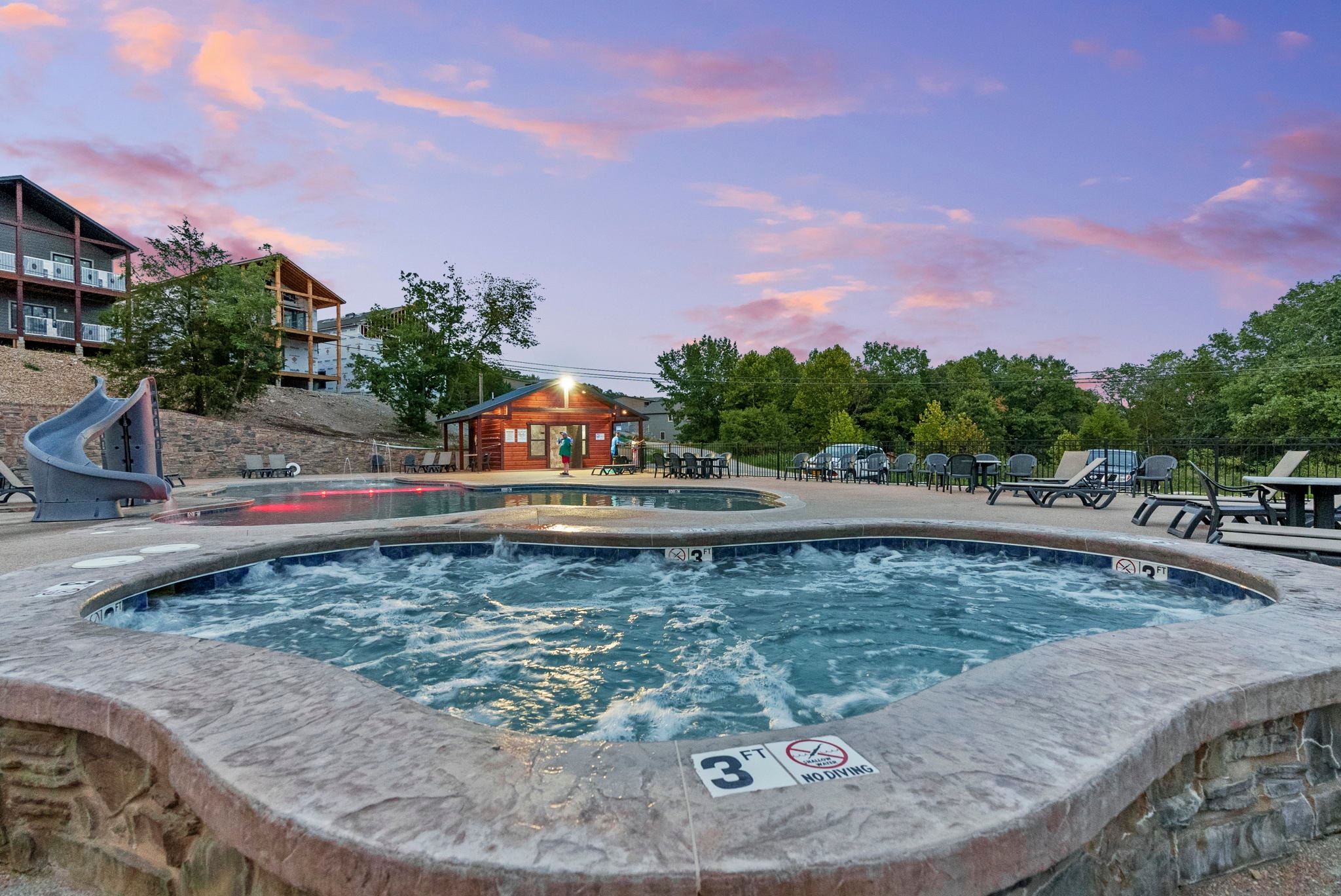 Resort pool, hot tub, and waterslide at sunset