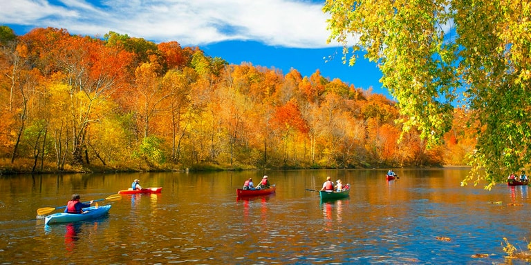 Canoes and kayaks paddling the James River through brilliant autumn foliage in the Ozarks