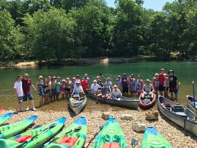 Large group of paddlers with canoes and kayaks gathered at a gravel bar on the White River